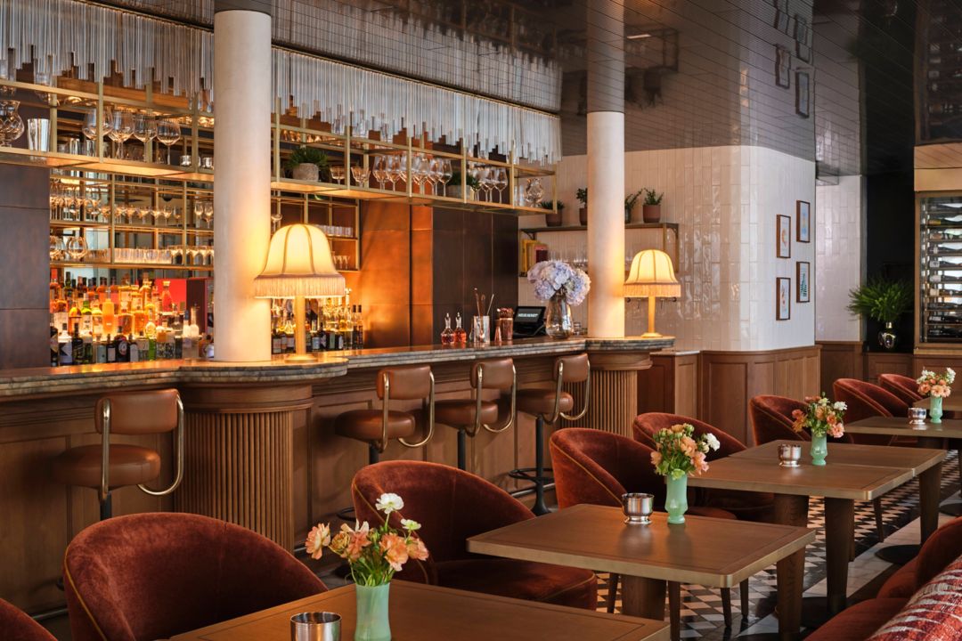 A Vienna bar with a well-stocked shelf of liquor bottles, bar stools, and tables with flowers.